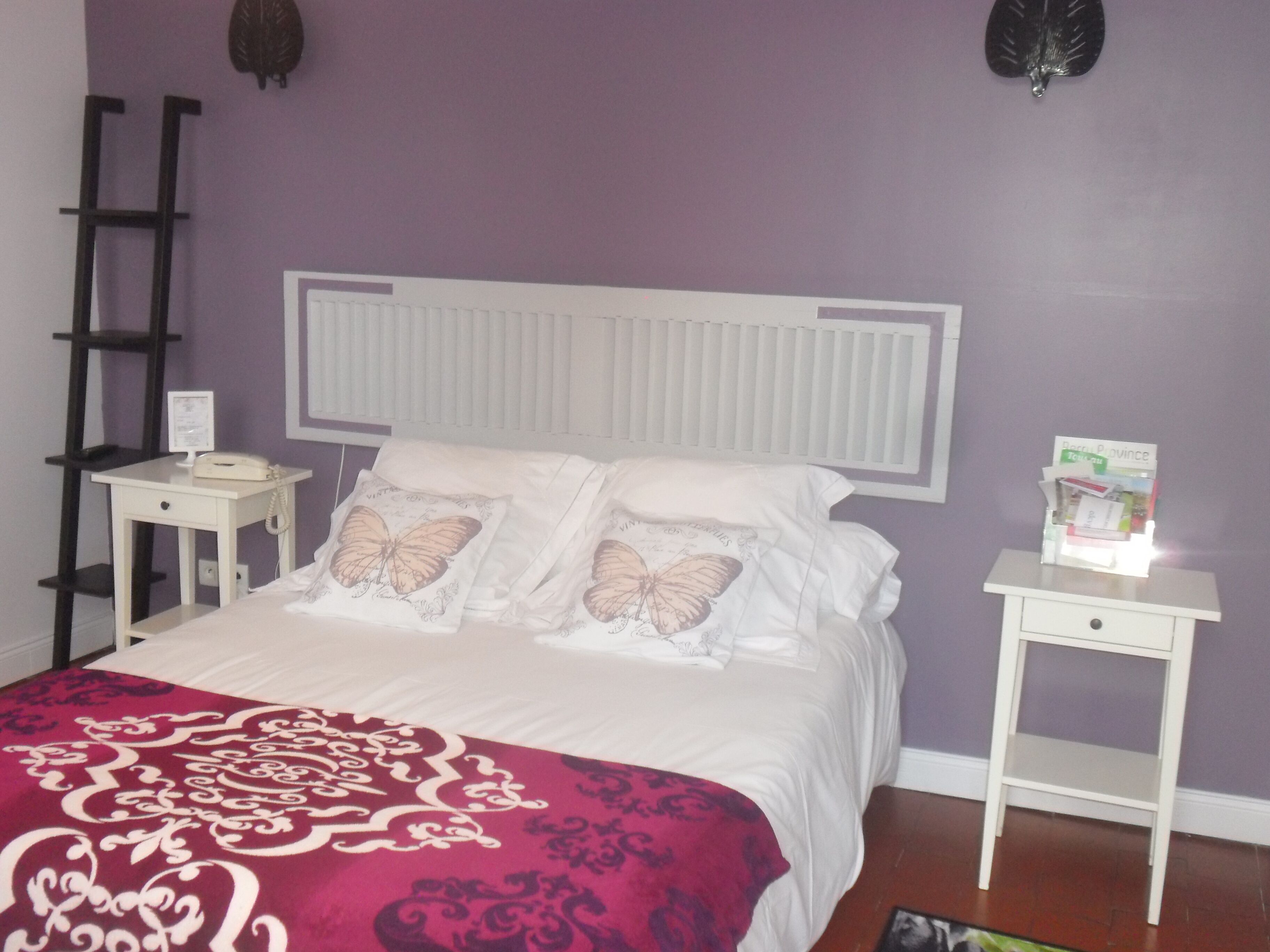 A bedroom with a bed, two bedside tables, a nightstand, a ladder, and a bulletin board on the wall.