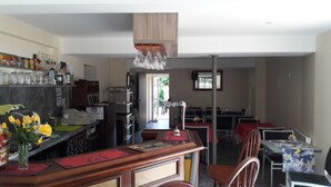 A restaurant with a bar area, dining tables, and chairs. There are flowers on the bar counter, and a ceiling light fixture above the bar. - Hotel La Buissonniere (Bannay)