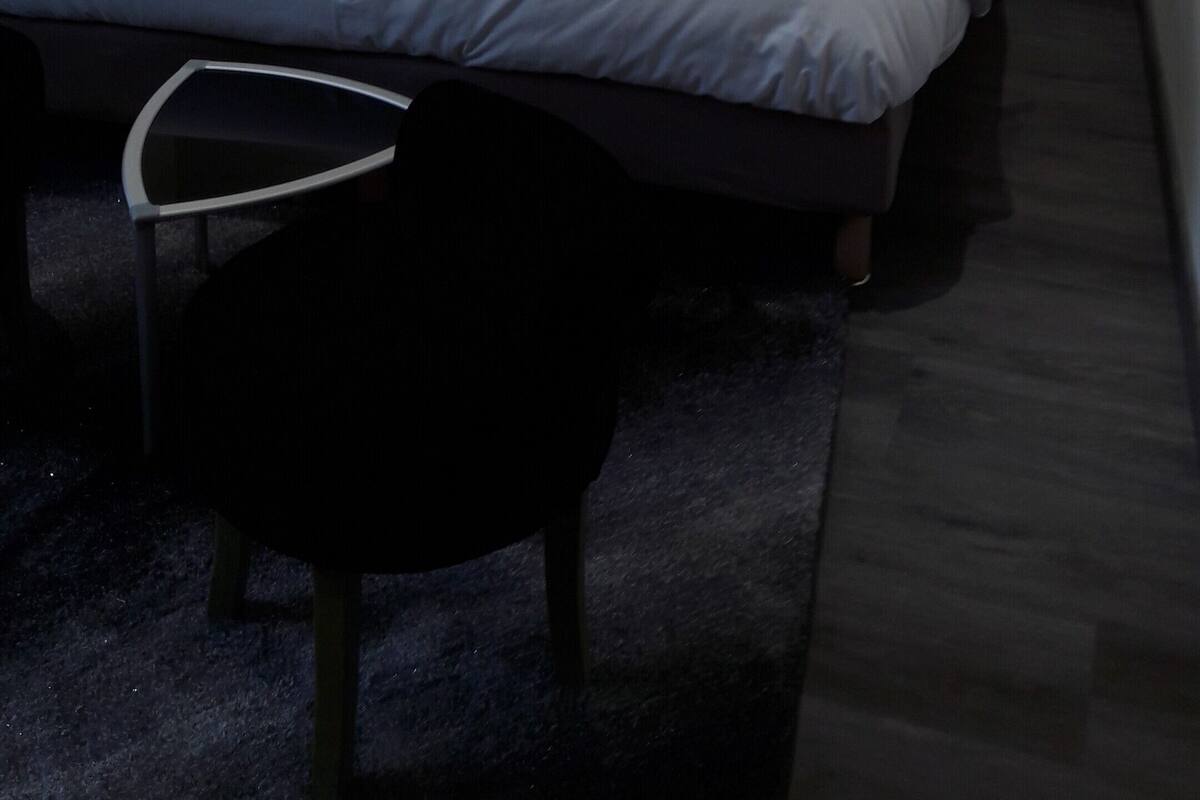 A modern bedroom with a bed, two bedside tables with lamps, a chair, and a textured wall.