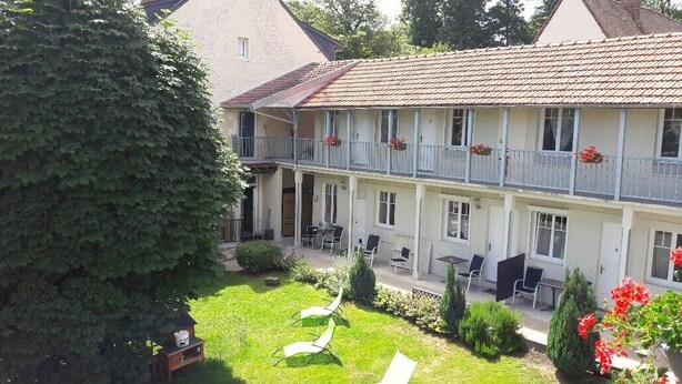 A two-story building with a balcony on the upper floor, a garden with chairs and tables, and a large tree in the foreground. - Hotel La Buissonniere (Bannay)