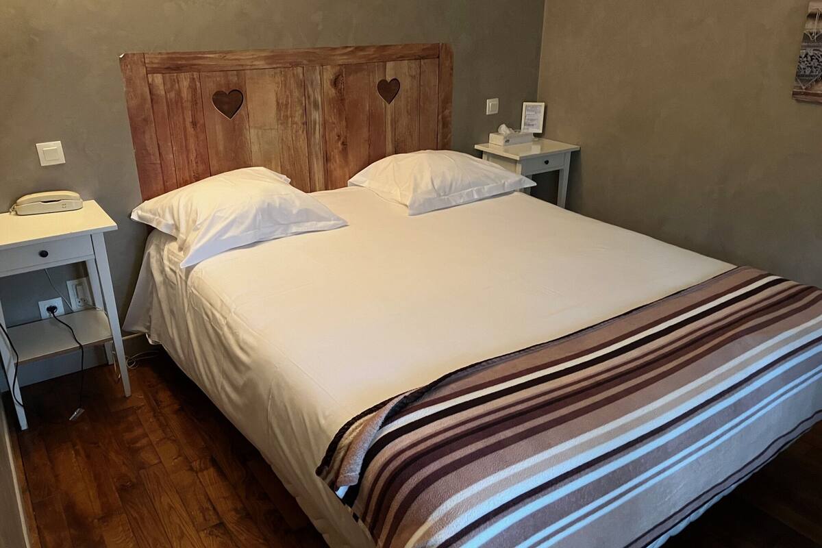 A neatly made bed with white linens and a striped blanket, a wooden headboard with heart-shaped cutouts, bedside tables with lamps, and a phone on the left table.