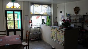 A small, brightly lit room with a tiled floor, a wooden table, a chair, a window with blinds, and a bulletin board with various papers and a map. - Hotel La Buissonniere (Bannay)