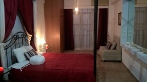 A bedroom with a bed, a chair, a nightstand, and a window with curtains. - VILLA WITH  PRIVE POOLGARDEN AREA, bbq , wi-fi,  near sea , town, local tavern (rethymno)