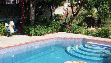 Una piscina con superficie d'acqua cristallina e azzurra, circondata da vegetazione lussureggiante e alberi.