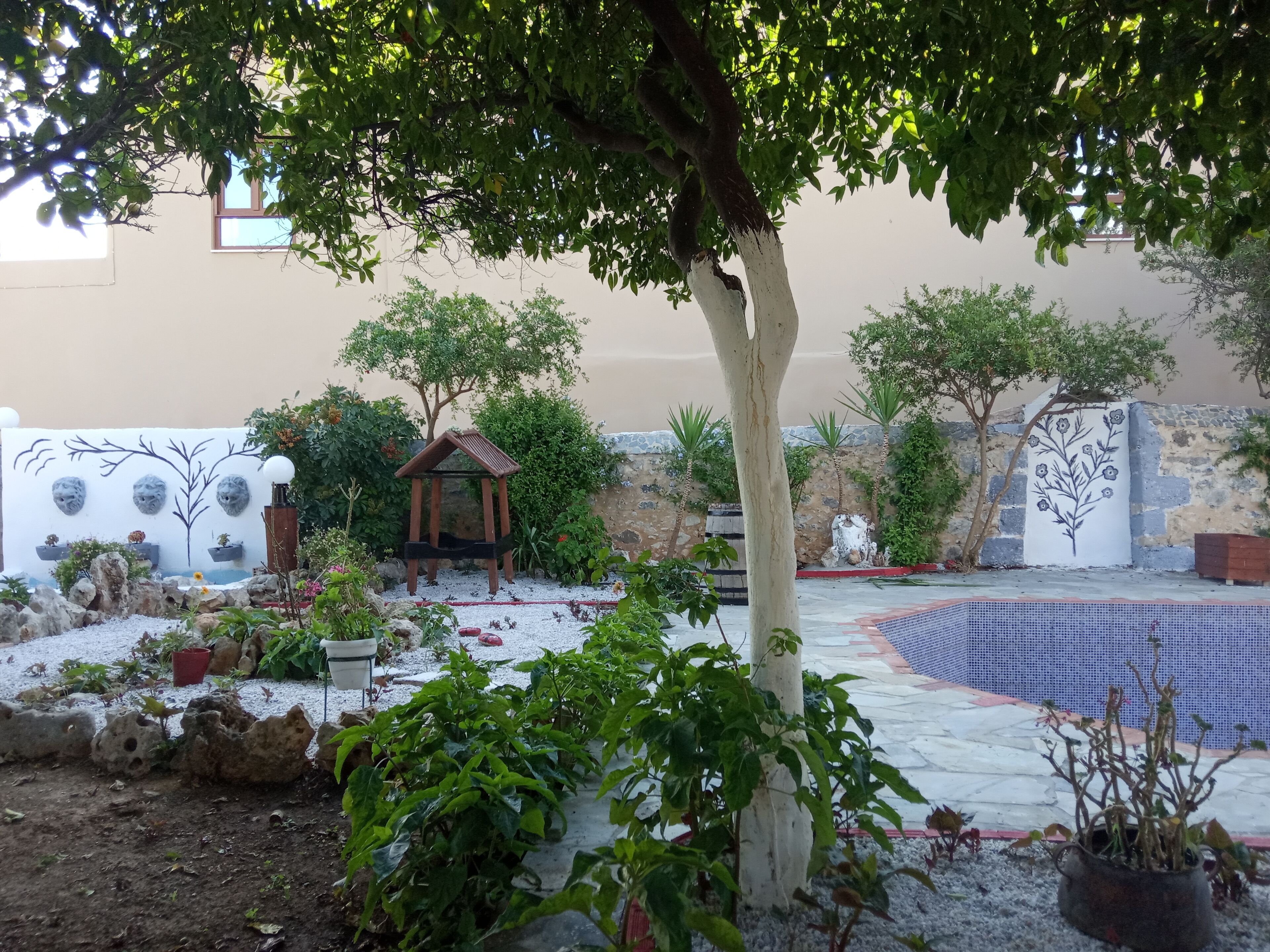 A garden with a wooden gazebo, potted plants, and a decorative wall.