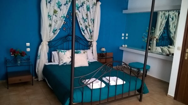 Quarto com cama de dossel, mesa de cabeceira, espelho e um pequeno banquinho.