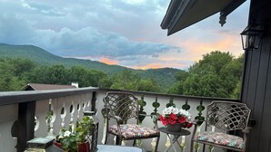 Un balcón con vista a un paisaje montañoso, dos sillas, una mesita y plantas en macetas.