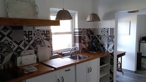 A kitchen with white cabinets, a wooden countertop, a sink, a coffee maker, and two hanging lights.