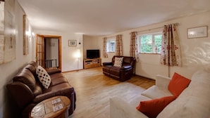 A living room with a brown leather sofa, a white sofa, a wooden coffee table, a television, and a radiator. - Hop Cottage (Ashford)