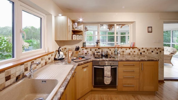 A modern kitchen with wooden cabinets, a granite countertop, and a built-in oven. - Hop Cottage (Ashford)
