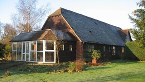 A wooden house with a large glass conservatory and a sloped roof. - Hop Cottage (Ashford)