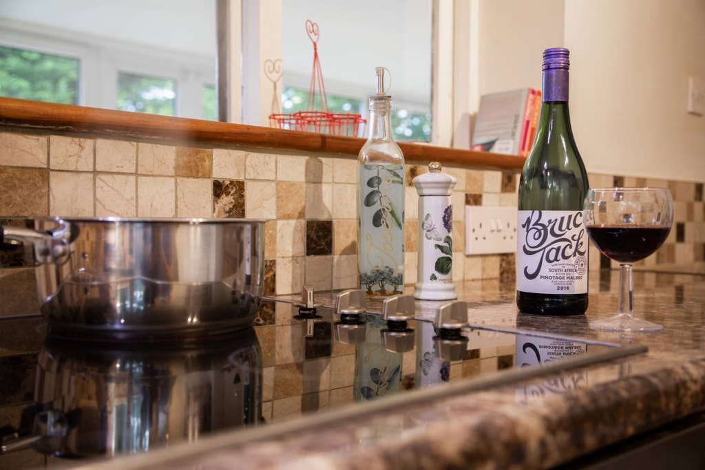 A kitchen counter with a wine bottle, a glass of wine, a teapot, and a decorative bottle.
