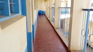 A corridor with blue and beige walls, a red floor, and metal railings on one side. - The Place Bar And Restaurant (Oyugis)