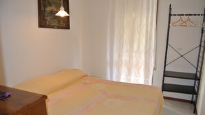 A bedroom with a bed, a wooden dresser, a hanging light fixture, and a metal rack with hangers. - Croce del Sud 39 - Lignano (Lignano Sabbiadoro)