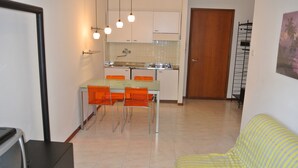 A compact living space with a kitchenette, dining area, and a sofa. - Croce del Sud 39 - Lignano (Lignano Sabbiadoro)