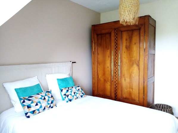 A bedroom with a bed, two pillows, a wooden wardrobe, and a woven light fixture. - 3* renovated house, large garden, close to beaches (Trébeurden)