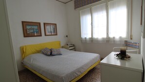 Un dormitorio con cama, escritorio, silla, lámpara y dos cuadros en la pared.