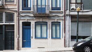 A building with a blue door and windows, a black car parked in front, and a street lamp.