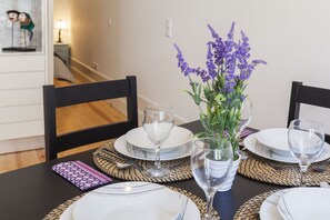 A dining table set with white plates, clear wine glasses, and a vase with purple flowers. - Fantastic Apartment in Porto Center Completely Renovated! (porto)