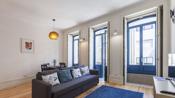 A modern living room with a grey sofa, blue patterned rug, and a dining area with a table and chairs.