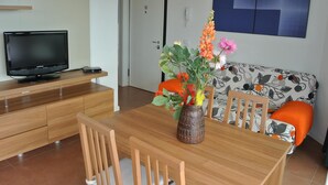 A modern living room with a wooden dining table, a sofa with a floral pattern, a television on a wooden cabinet, and a vase with flowers. - KATRINA 2 - Lignano Sabbiadoro (Lignano Sabbiadoro)
