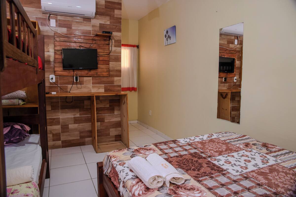 Un dormitorio con una cama, un escritorio de madera, un televisor montado en la pared y un espejo.