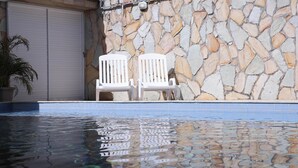 A pool area with two white chairs and a stone wall. - Pousada Meu Xodó (São Miguel dos Milagres)