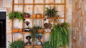 A wooden shelf unit with plants and decorative items against a stone wall. - Pousada Meu Xodó (São Miguel dos Milagres)