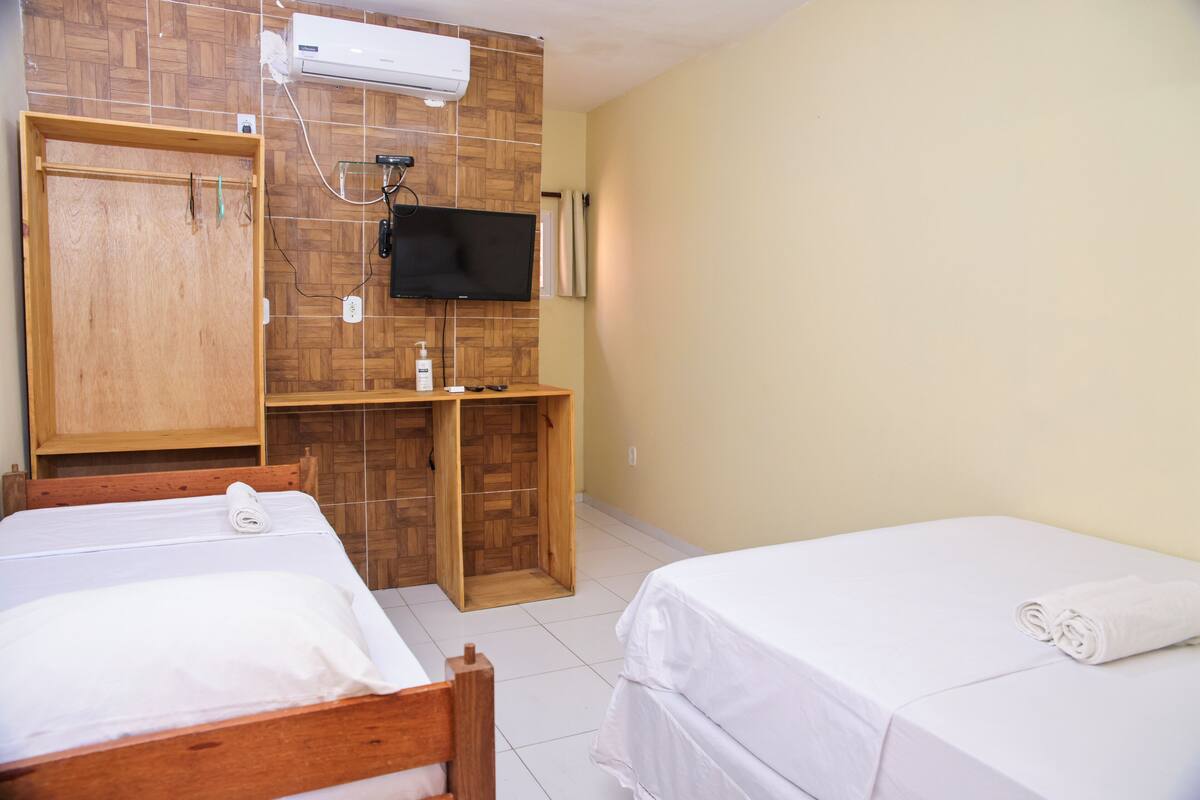 Una habitación de hotel con dos camas, un armario de madera, un escritorio con televisor y un equipo de aire acondicionado.