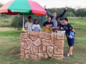 Un grup de persones al voltant d'una zona de bar exterior amb pedra i un parasol de colors.