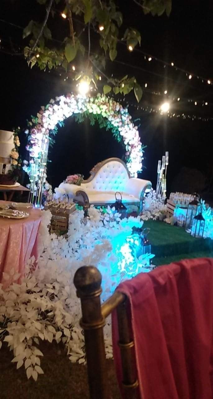 Decoració de boda a l'aire lliure, amb una arcada floral, un sofà blanc i una zona de menjador.
