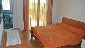 A bedroom with a wooden bed, a bedside table, and a view of the outside through a window with curtains.