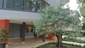 A modern building with a central courtyard featuring a large tree, potted plants, and a well-maintained lawn.