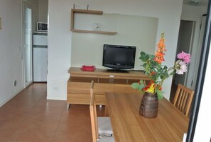 A modern kitchen with a wooden table, chairs, a TV, and a vase with flowers.