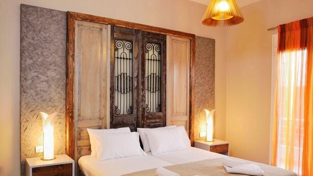 Een hotelkamer met een groot bed, twee bedlampen, een houten hoofdbord en een raam met oranje gordijnen.
