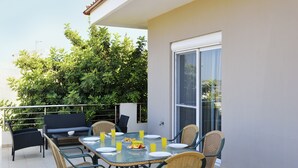 Een balkon met een eettafel voor vier personen, omringd door rieten stoelen, een bank en een barbecue.