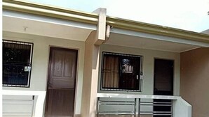 A building with a brown door, two windows with metal bars, and a white railing on a stone-paved area. - Ferrer's Villa Apt 3 close to beaches, parks, banks, market and parks. (Romblon Odiongan)