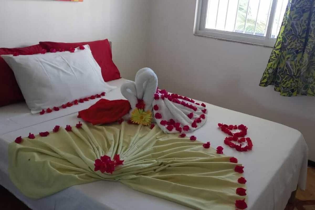 A neatly made bed with a white and red color scheme, a decorative towel arrangement, and a floral centerpiece.