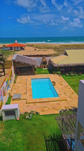 A pool area with a clear view of the ocean, surrounded by buildings with thatched roofs.