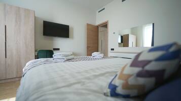 A hotel room with a bed, a TV mounted on the wall, a wardrobe, and a mirror.