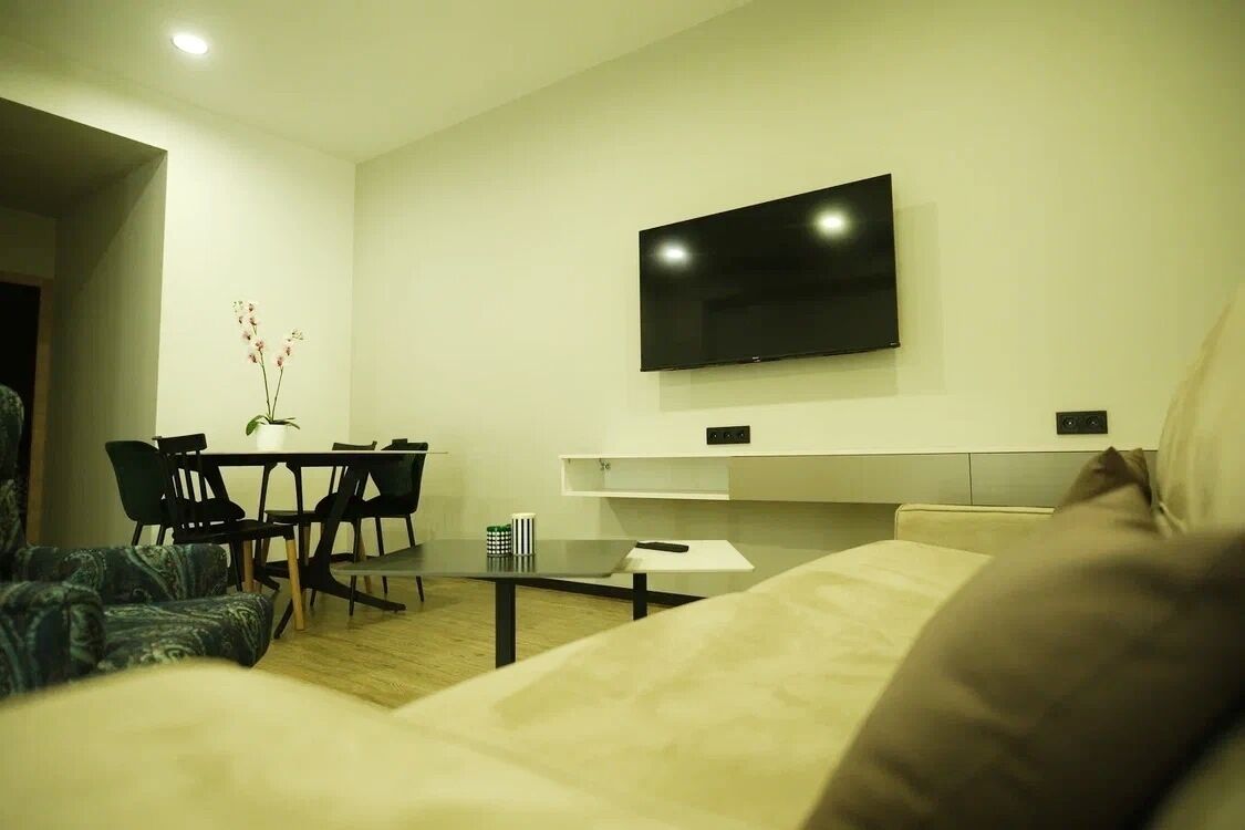 Een moderne woonkamer met een flatscreen televisie aan de wand, een eethoek met een tafel en stoelen, en een bank.