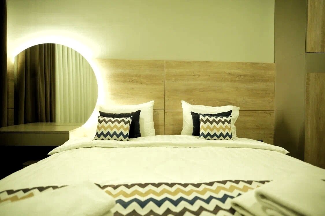 A hotel room with a wooden headboard, two pillows with zigzag patterns, and a circular light fixture on the wall.