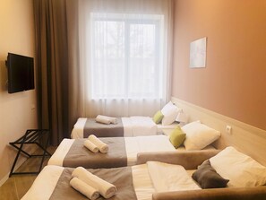 Hotellihuone, jossa on kaksi sänkyä, seinälle asennettu televisio ja ikkuna, jossa on läpikuultavat verhot.