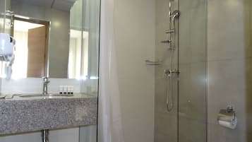 Un bagno moderno con cabina doccia in vetro, piano di lavoro in granito e porta carta igienica a vista.