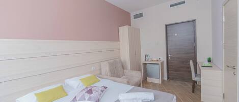 A hotel room with a bed, a desk, a wardrobe, and a door.