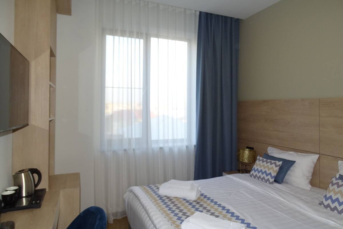 Hotellihuone, jossa on sänky, televisio, kahvinkeitin ja ikkuna, jossa on verhot.