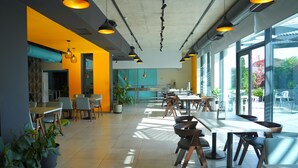 Een moderne eetruimte met tafels, stoelen, grote ramen en potplanten.