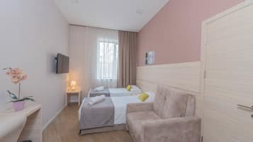 Een hotelkamer met twee bedden, een bank, een televisie, een raam met gordijnen en een bloempot met plant.