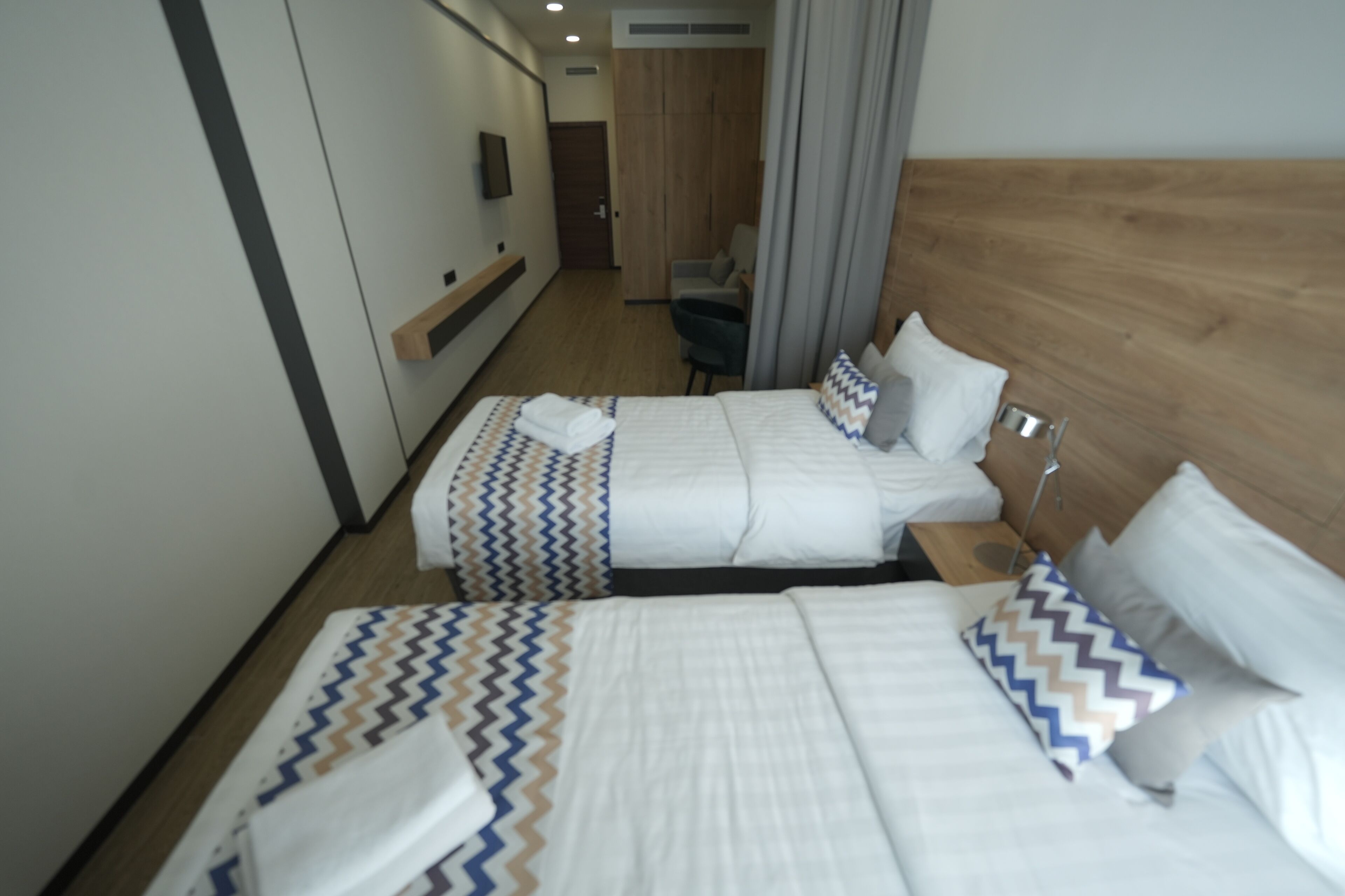 Une chambre d’hôtel avec deux lits, une tête de lit en bois, une télévision et un bureau avec une chaise.