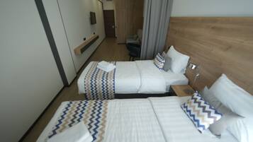 Une chambre d’hôtel avec deux lits, une tête de lit en bois, une télévision et un bureau avec une chaise.